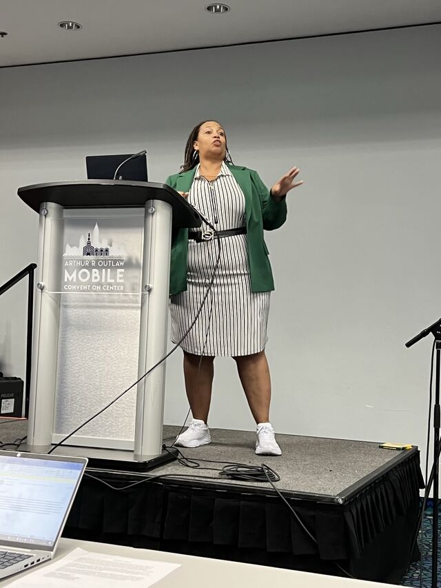 Hedreich presenting from a podium in a green blazer